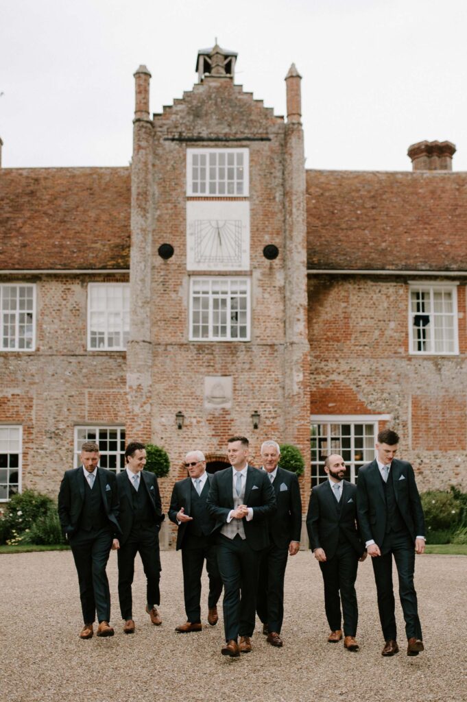 Photo of groomsmen standing and joking together outside Bruisyard Hall