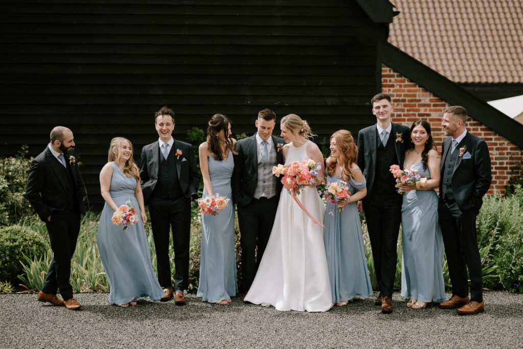 Bride standing with her bridesmaids in front of the barn at Bruisyard Hall