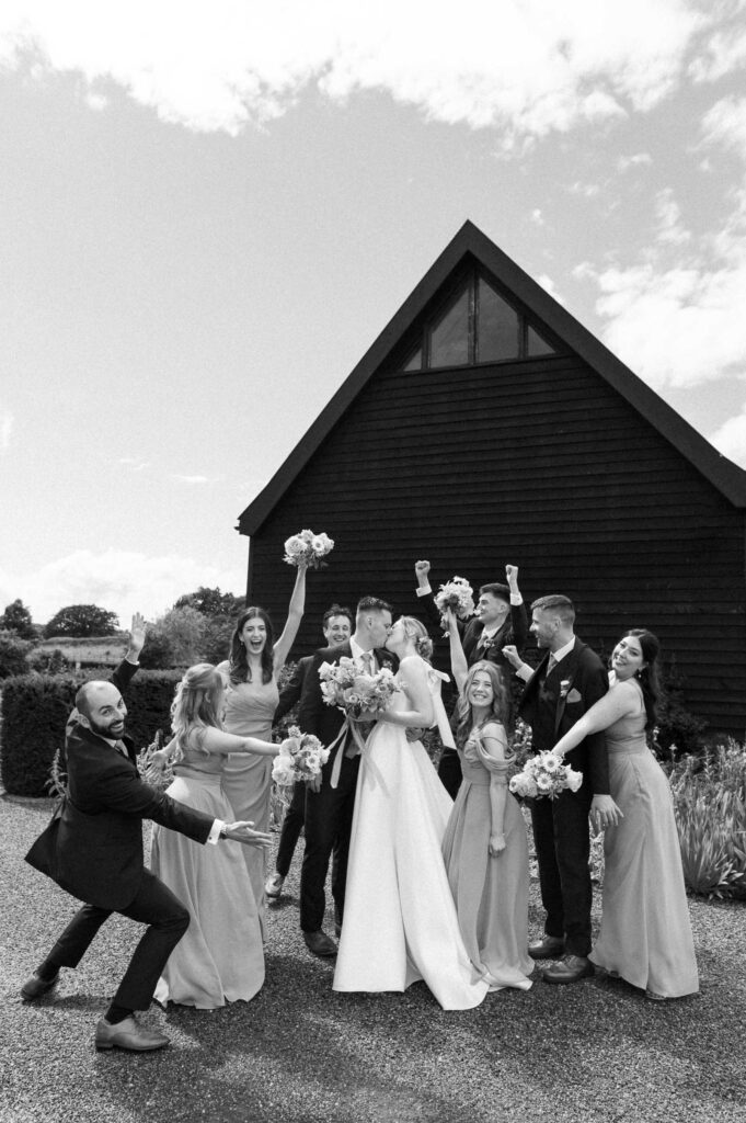 Bride Heidi and her bridesmaids standing together holding bouquets in front of the barn at Bruisyard Hall