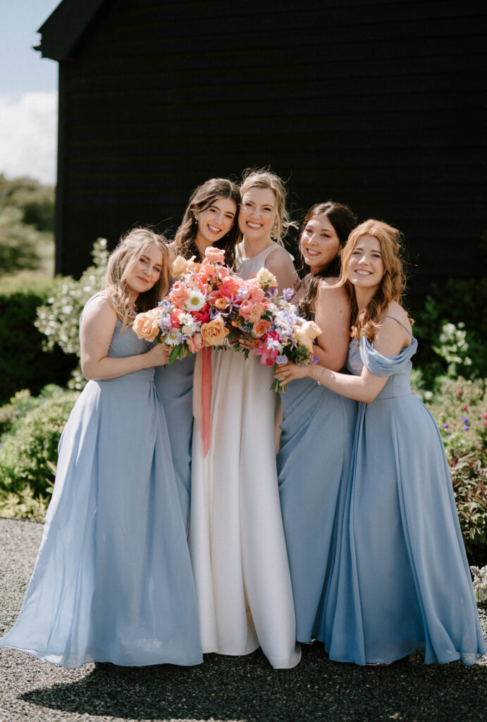 Bride standing with her bridesmaids holding bouquets outside at Bruisyard Hall