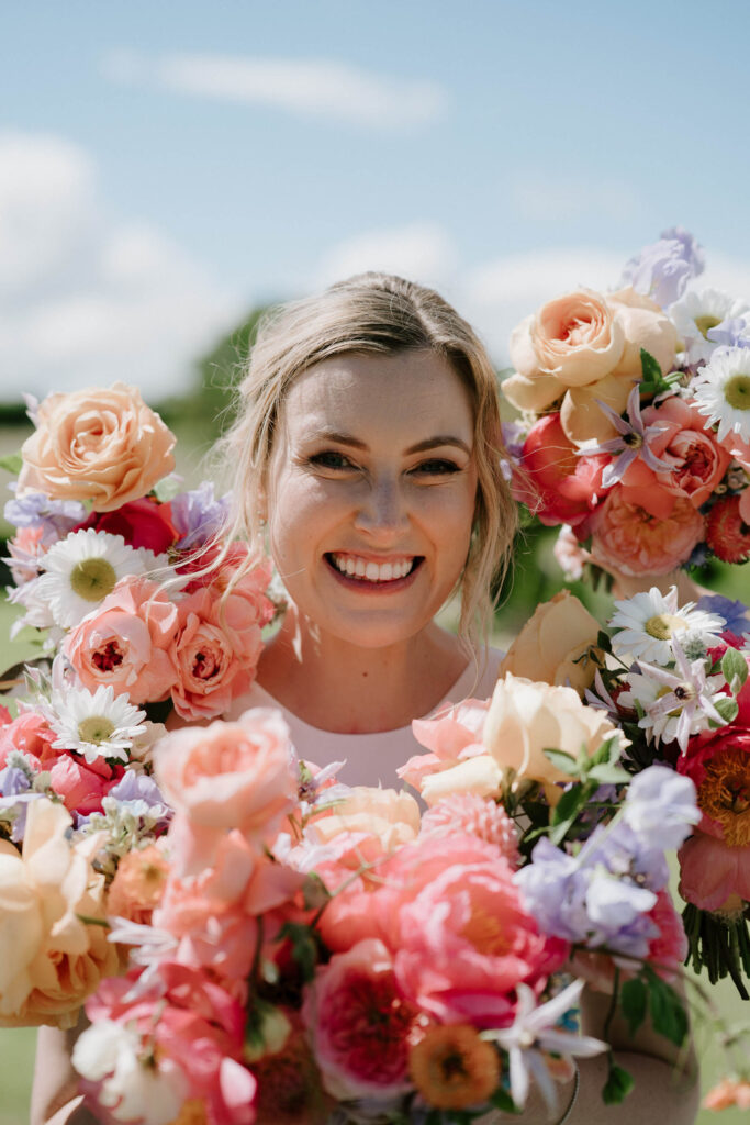 Close-up portrait of bride smiling with bridesmaid bouquets at Bruisyard Hall