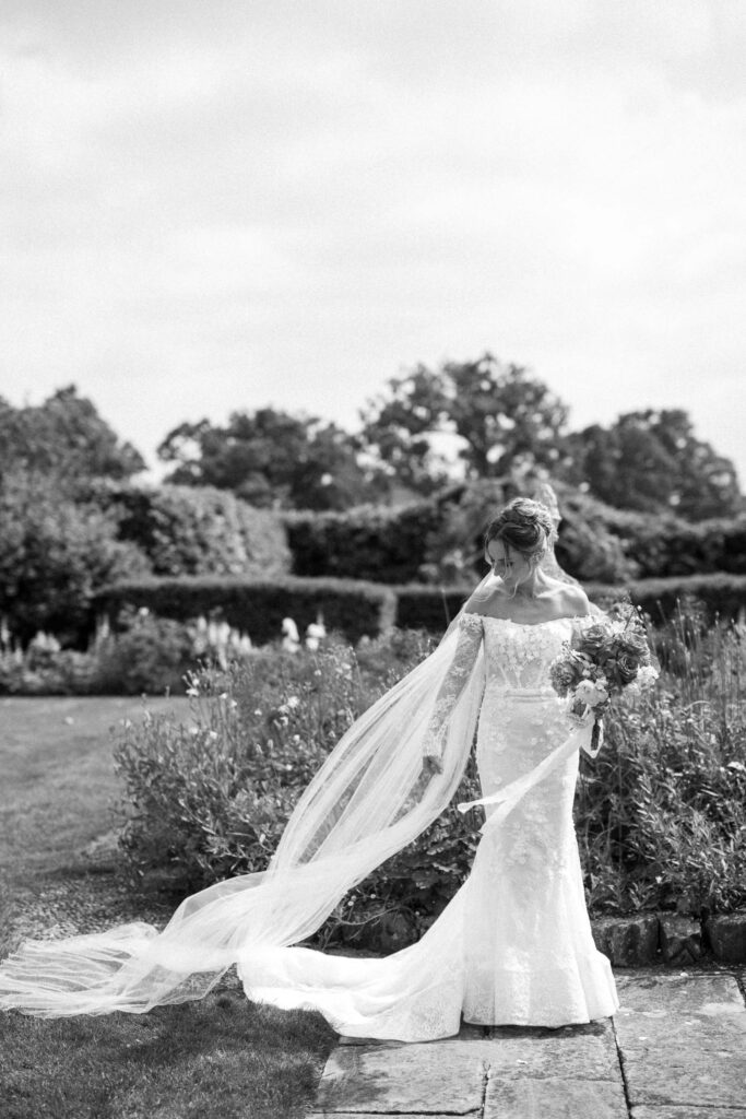 Bride walking through the gardens at Butley Priory with her veil flowing behind her.