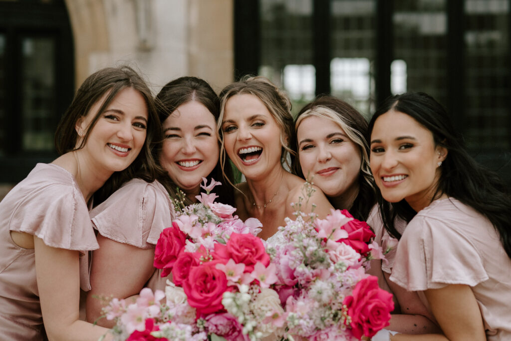 Bridesmaids smiling closely together holding pink wedding flowers.