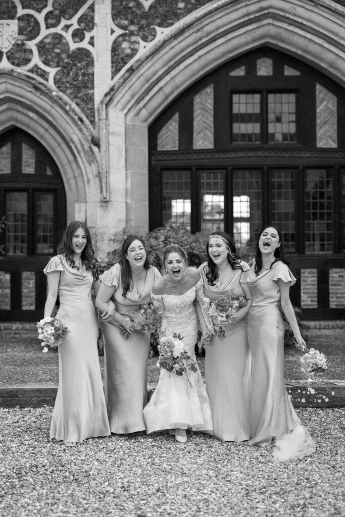 Bride and bridesmaids walking together and laughing outside Butley Priory.