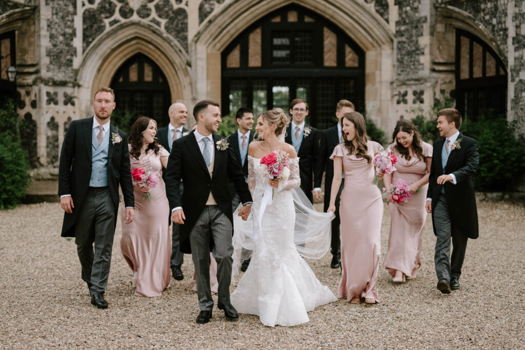 Bride and groom walking hand in hand with their wedding party outside Butley Priory.