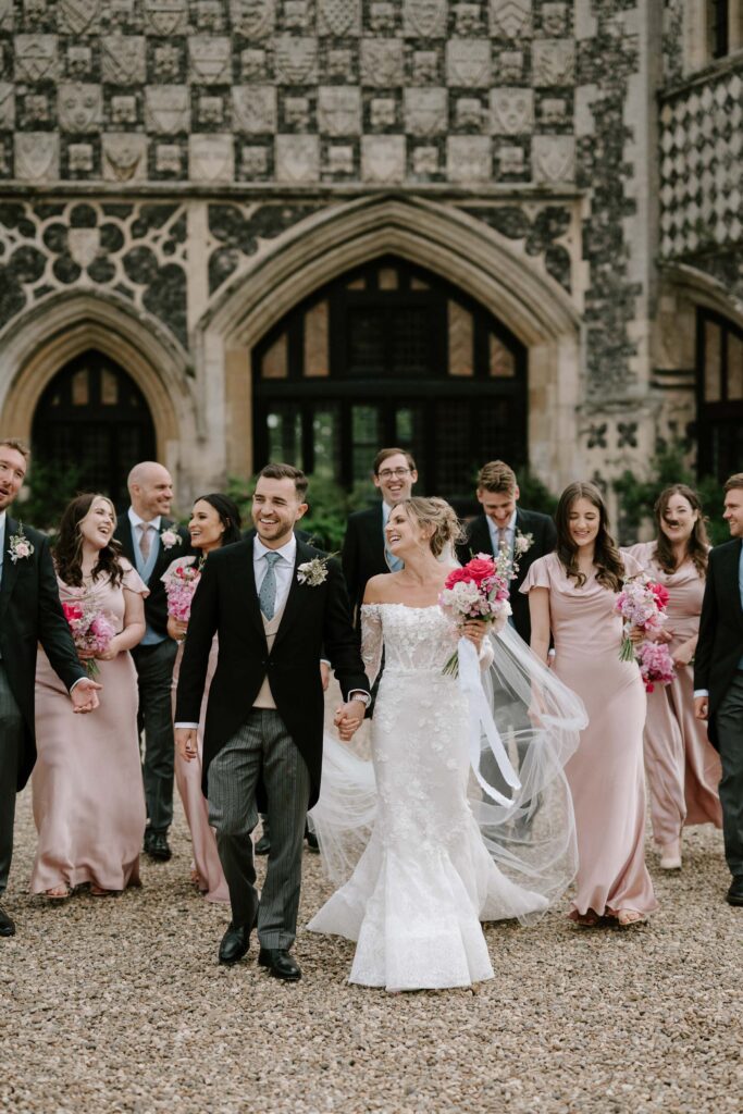 Bride and groom leading their bridesmaids and groomsmen outside Butley Priory after the ceremony.
