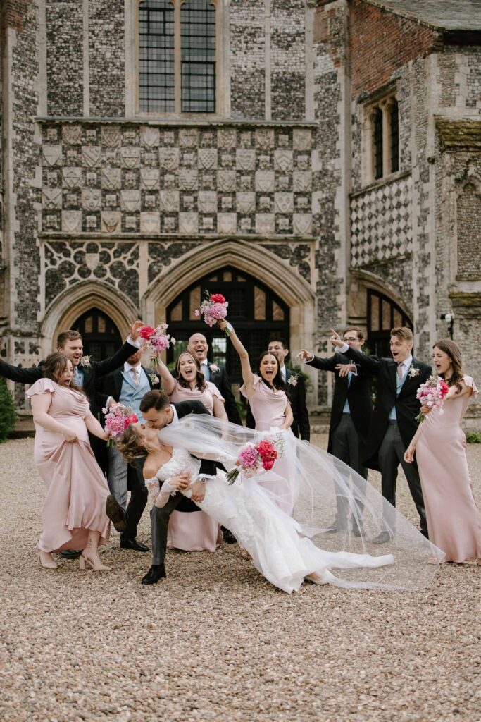 Bride being dipped by the groom as the wedding party celebrates outside Butley Priory