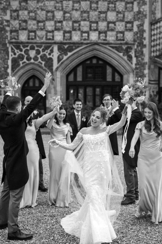 Bride celebrating joyfully with her wedding party outside Butley Priory.
