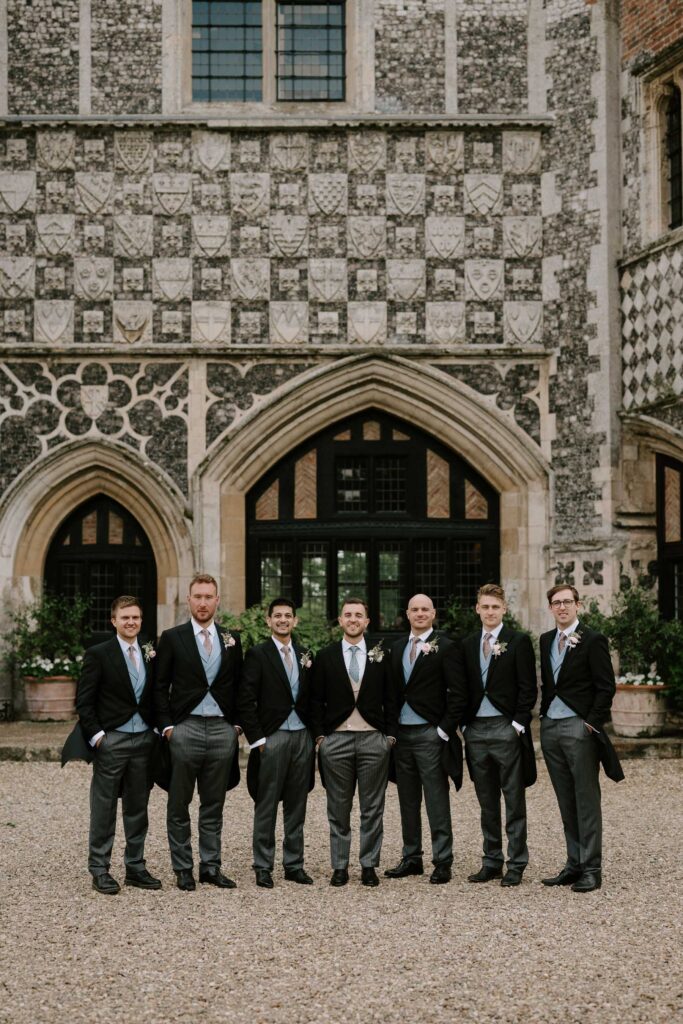 Groomsmen standing together outside Butley Priory during wedding group portraits.