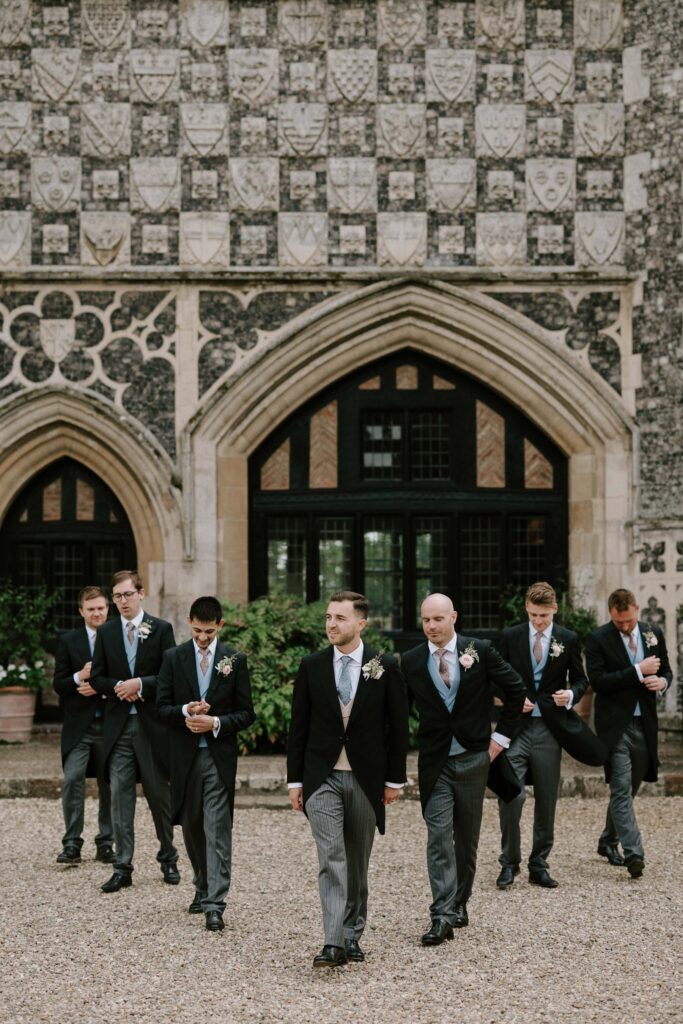 Groom walking forward with his groomsmen outside Butley Priory.