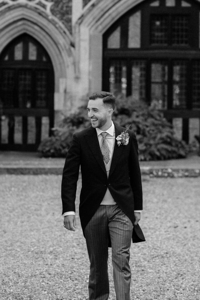 Groom walking and smiling outside Butley Priory during relaxed portraits.