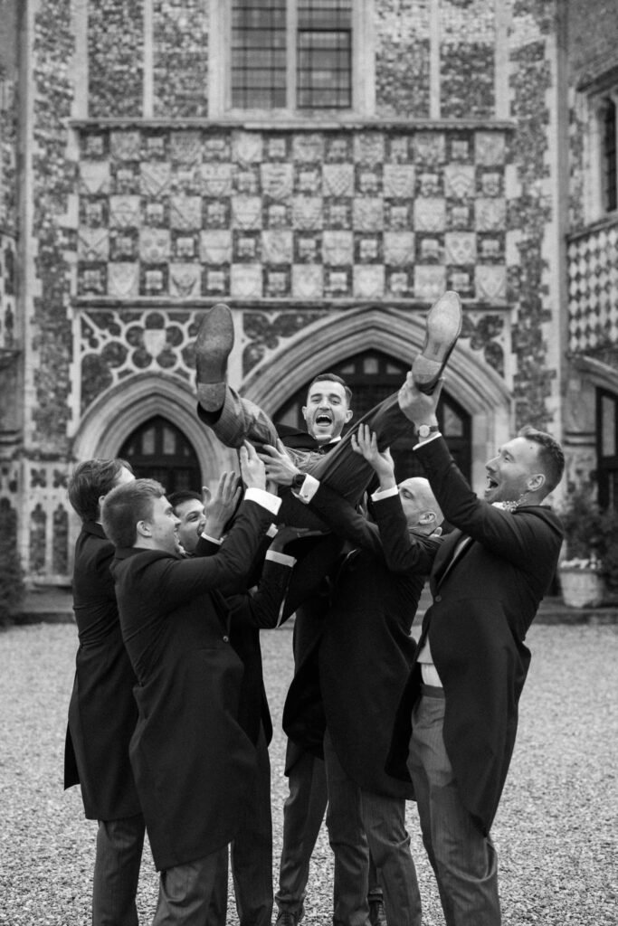 Groomsmen lifting the groom into the air during fun group photos 