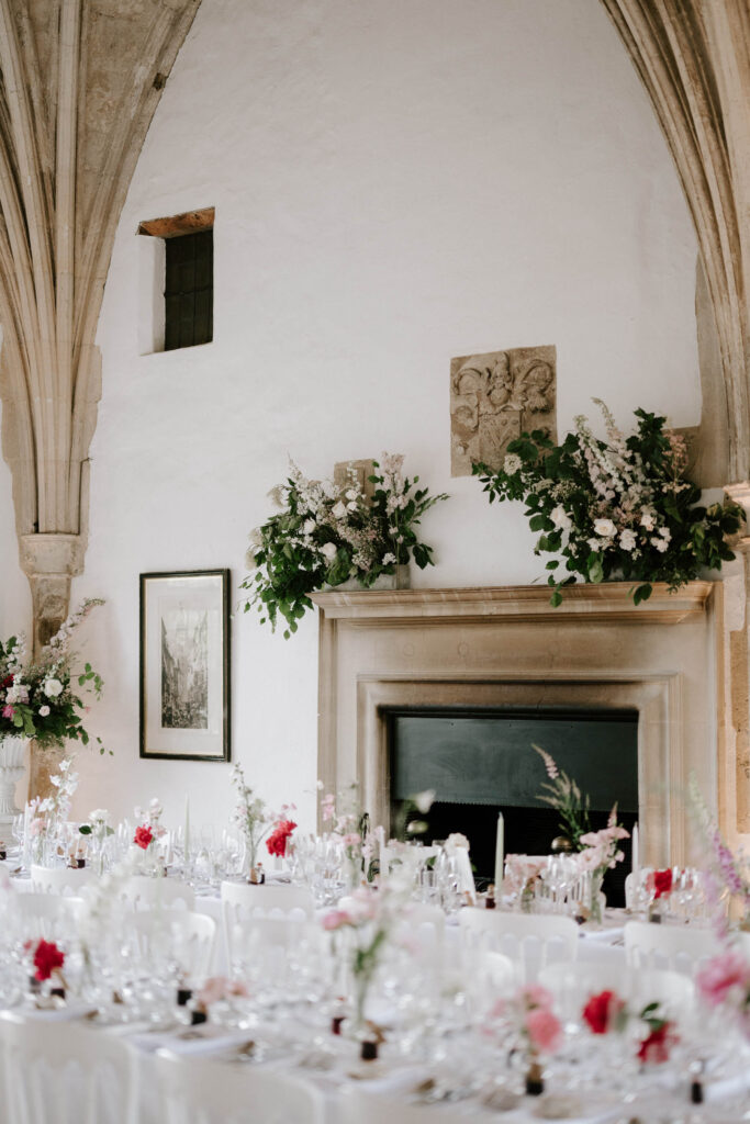 Wedding reception tables set with white linens and pink floral arrangements inside Butley Priory.