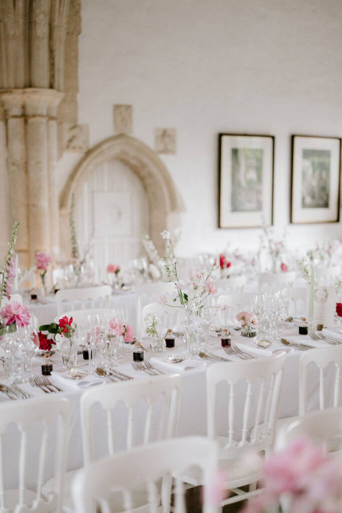 Long wedding reception tables styled with pink flowers and candles inside Butley Priory.