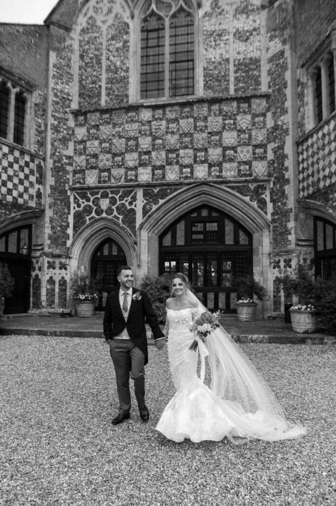 Bride and groom walking holding hands outside front at Butley Priory 