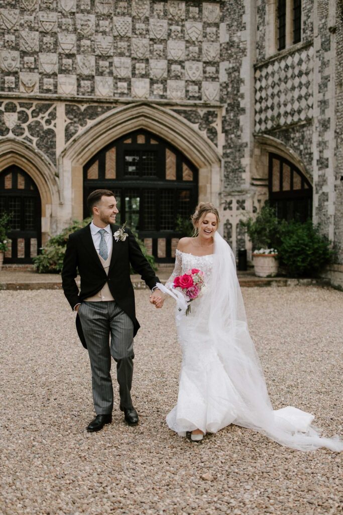 Bride and groom walking hand in hand outside Butley Priory during couple portraits.
