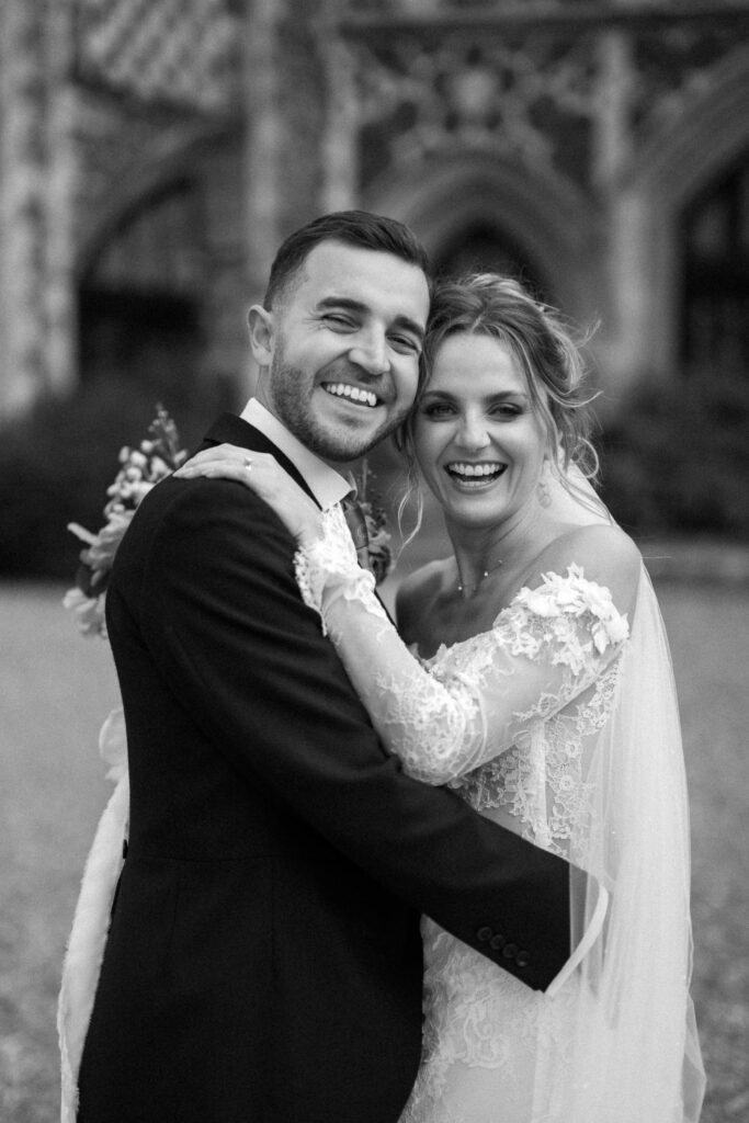 Bride and groom embracing and smiling together outside Butley Priory.
