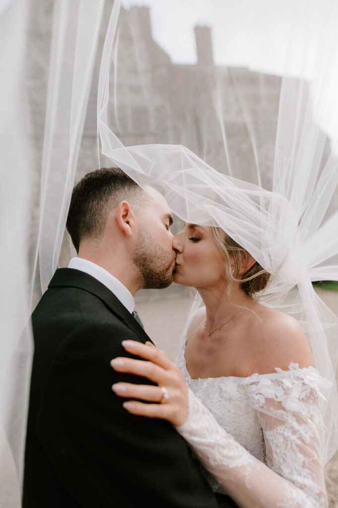 Bride and groom sharing a kiss beneath the bride’s veil outside Butley Priory.
