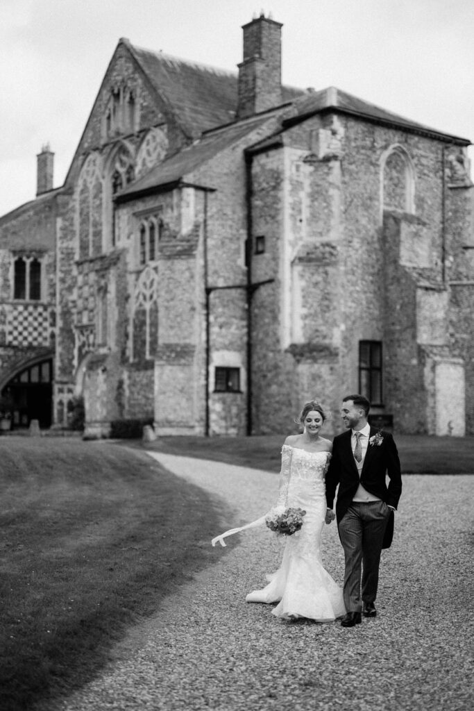 Bride and groom walking together in front of the historic Butley Priory building.