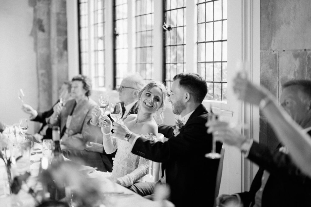 Bride and groom raising glasses during wedding speeches inside Butley Priory.