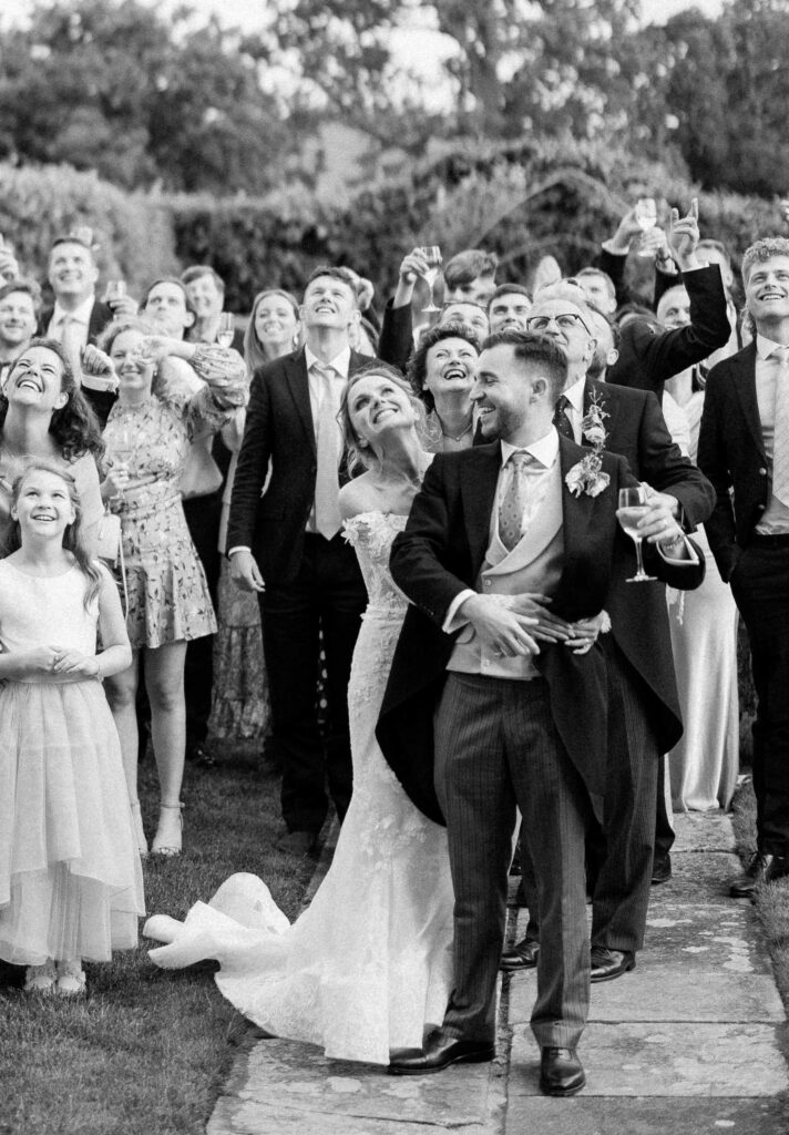 Bride and groom surrounded by wedding guests during a celebratory group moment.