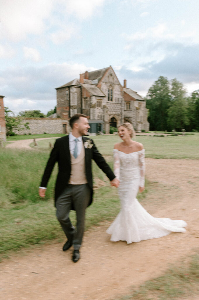 Bride and groom walking together in front of Butley Priory during couple portraits.