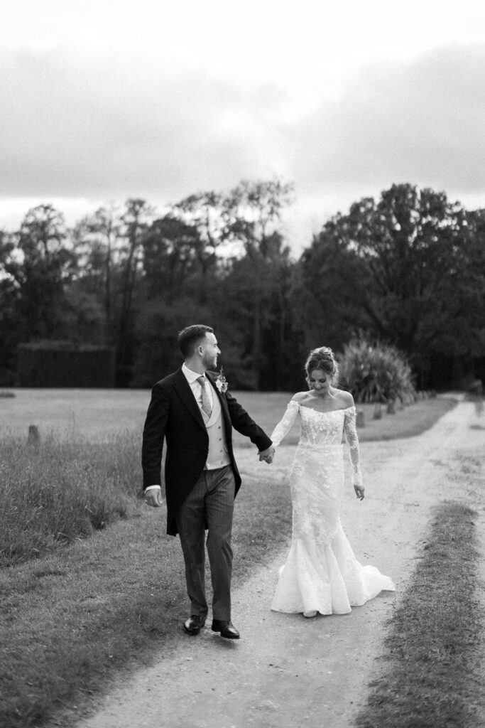 Bride and groom walking together along a path at Butley Priory.