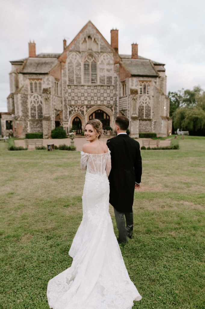 Bride and groom walking away together across the grounds of Butley Priory.