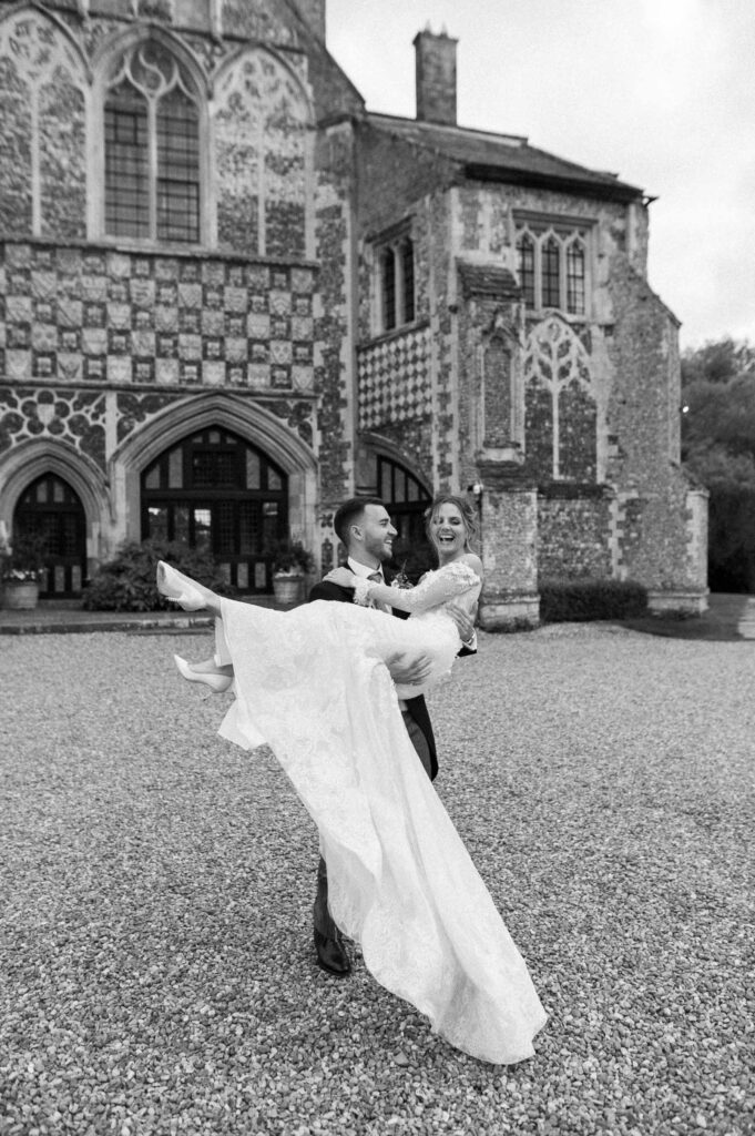 Bride being held in the groom’s arms outside Butley Priory.
