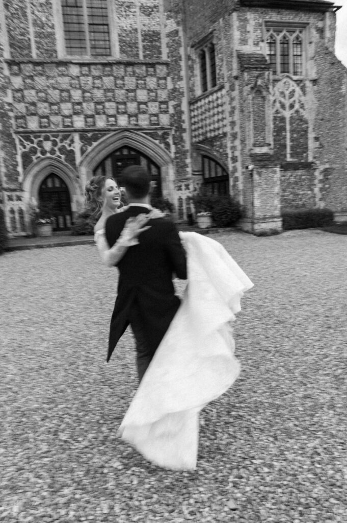 Groom lifting the bride and spinning her outside Butley Priory during couple portraits.