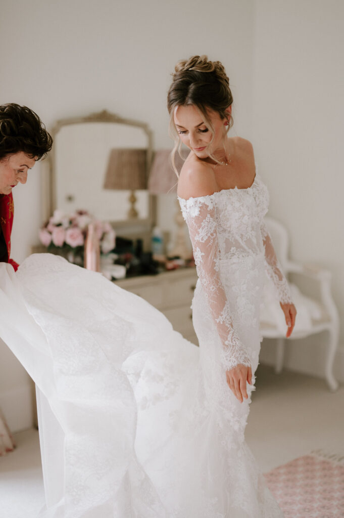 Bride having her wedding dress adjusted during morning preparations at Butley Priory.