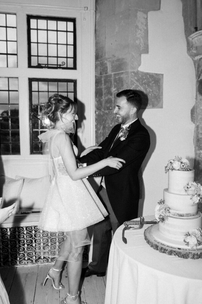 Bride and groom laughing together beside their wedding cake.