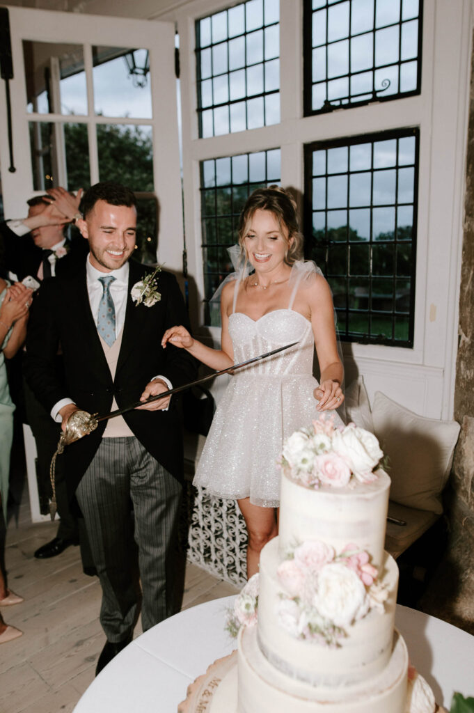 Bride and groom laughing together beside their wedding cake.