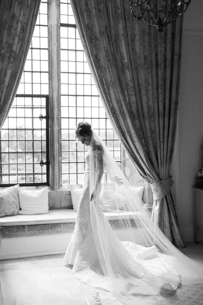 Bride standing by a large window during bridal prep at Butley Priory, wearing her wedding dress and veil.