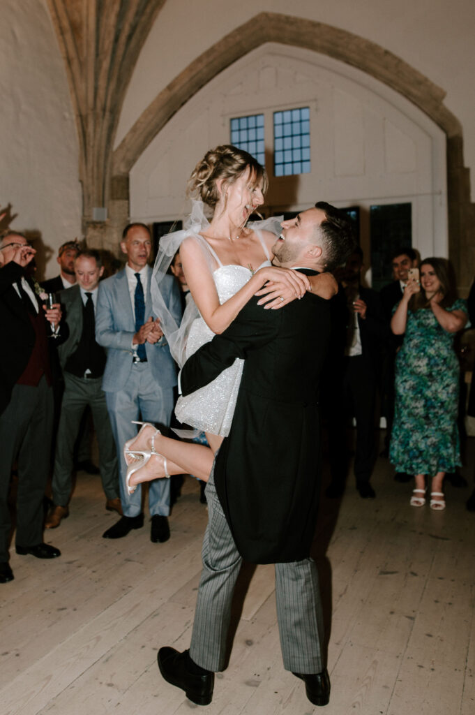 Groom lifting the bride as guests cheer during the wedding party.