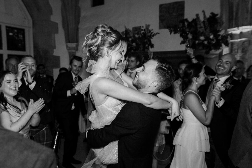 Bride and groom embracing on the dance floor surrounded by wedding guests.