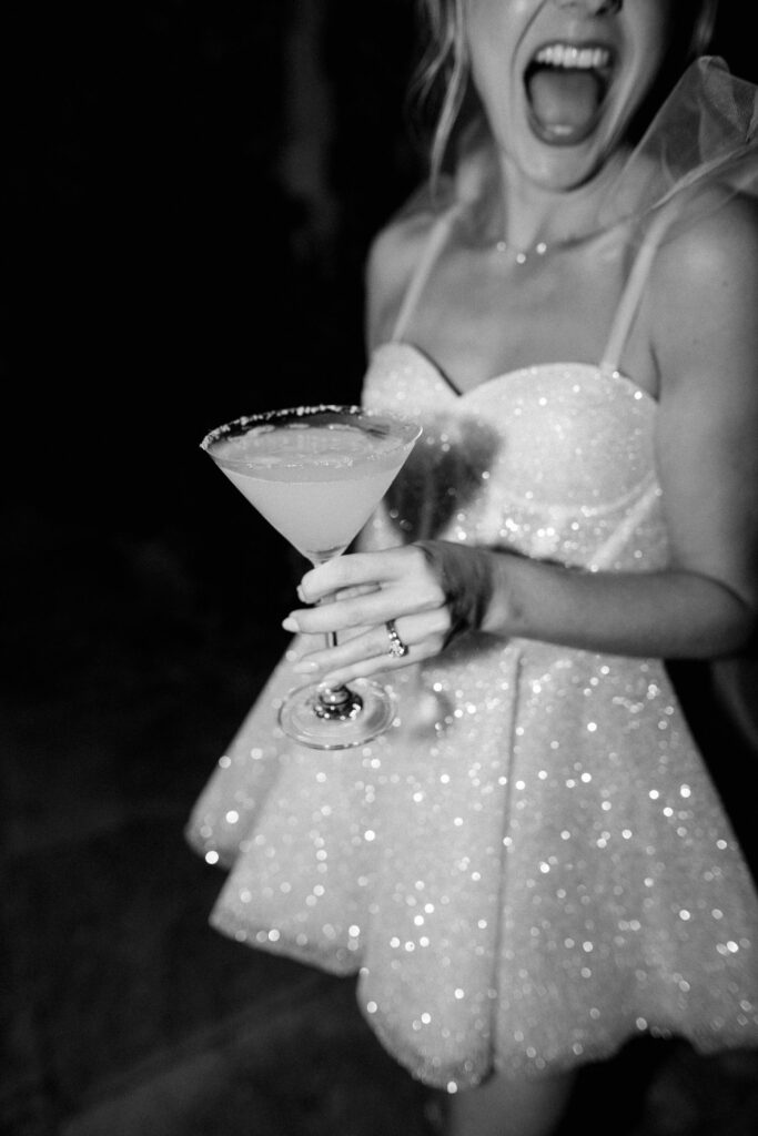 Bride holding a cocktail while wearing her short evening wedding dress.