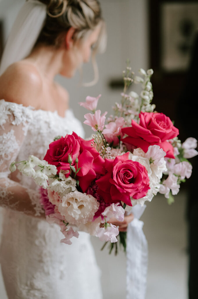 bride holding pink and white rose bouquet with silk ribbon and looking away