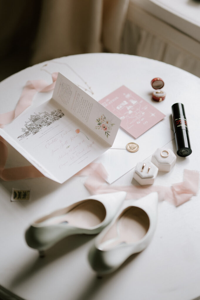 Flatlay of wedding morning details including perfume, jewellery, shoes and invitations at Butley Priory.