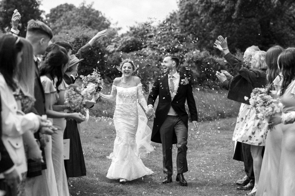 Bride and groom walking together through confetti moments after their wedding ceremony.