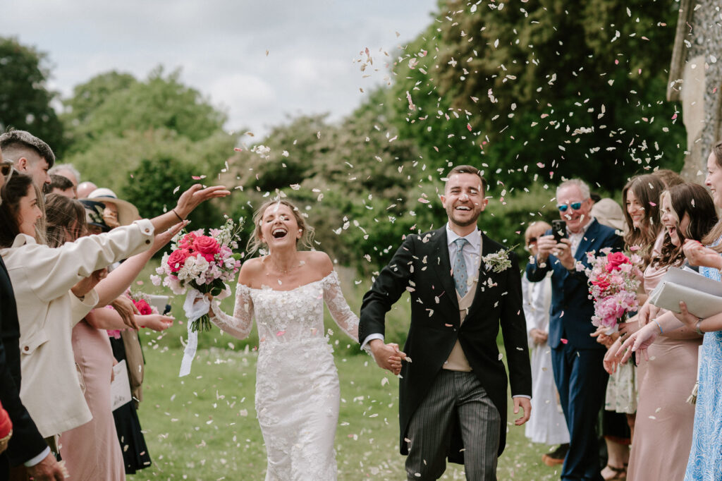 Bride and groom running hand in hand through a confetti line of wedding guests.