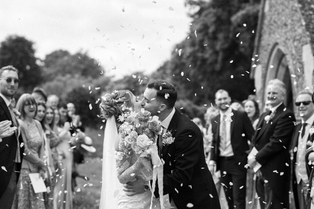Bride and groom laughing as confetti falls around them outside the church.
