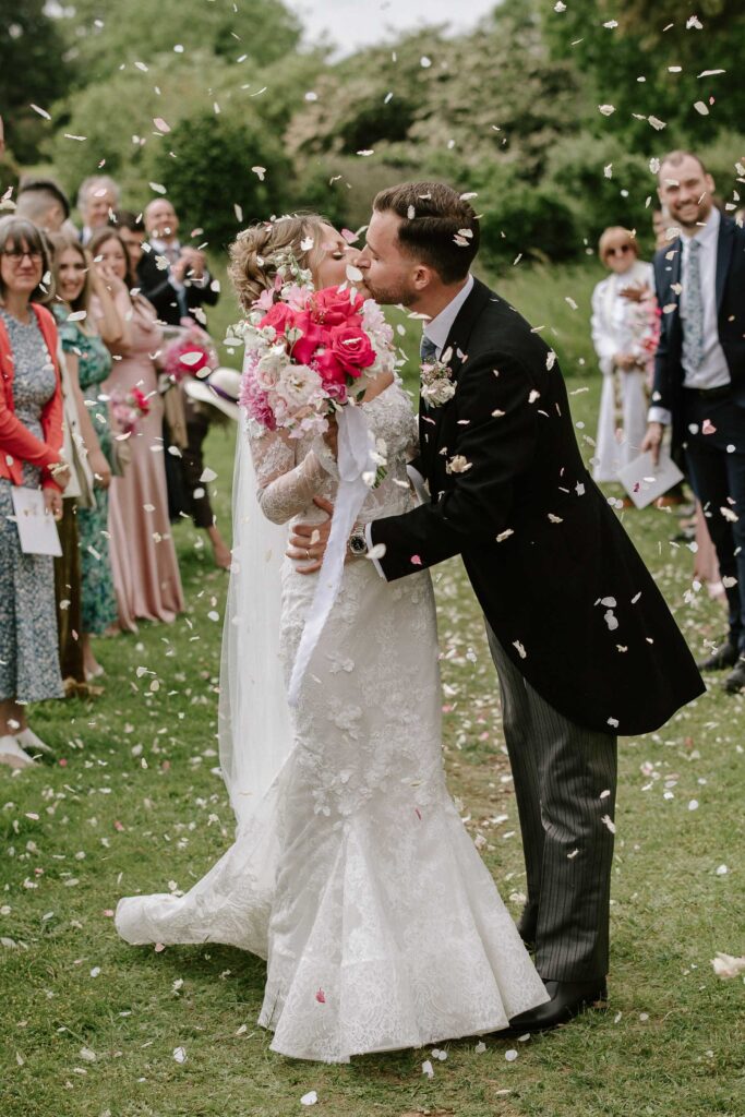 Bride and groom sharing a kiss during their confetti exit after the ceremony.