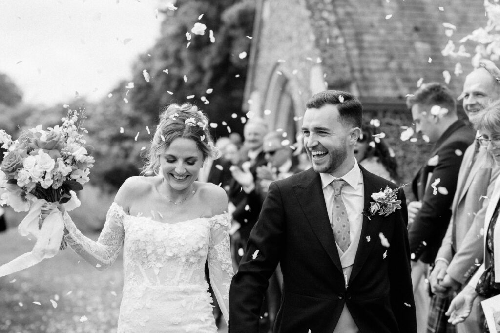 Bride and groom smiling as guests throw confetti outside the church.