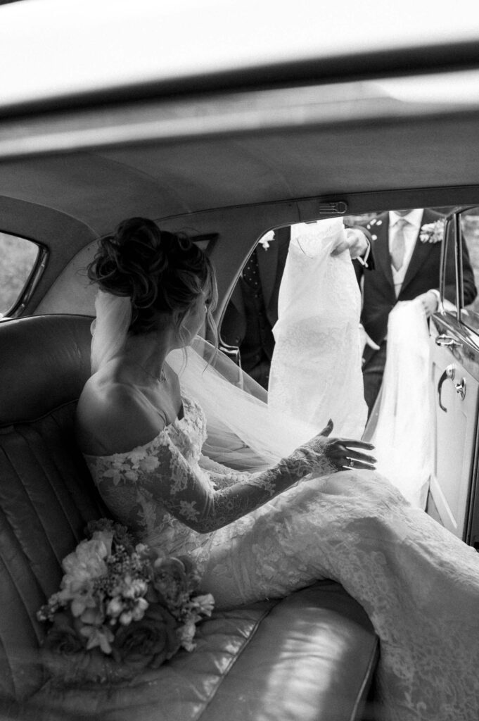 Bride sitting in the back of a vintage car wearing her wedding dress and veil.