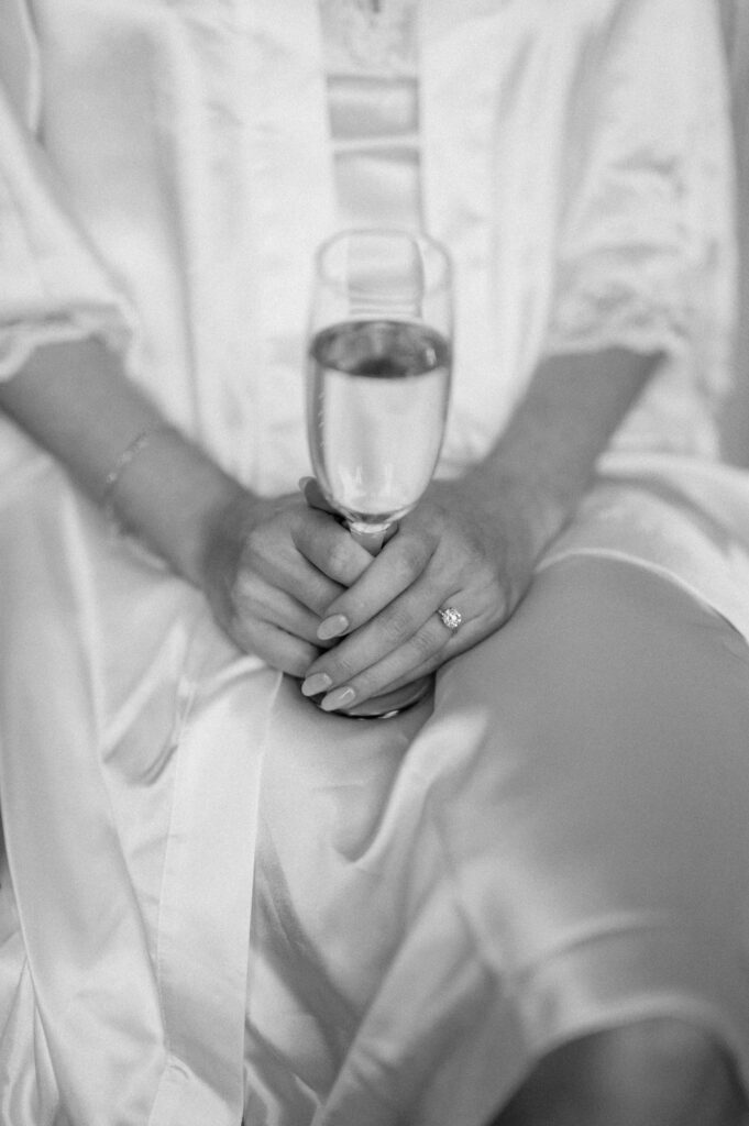 bride holding glass of champagne wearing silk robe on wedding morning at butley priory
