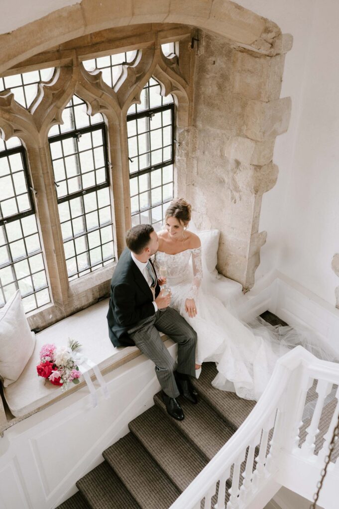 Bride and groom sitting together in a window alcove inside Butley Priory.