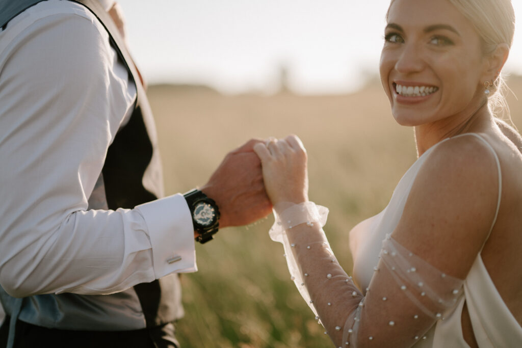 Close up of bride and groom holding hands during golden hour