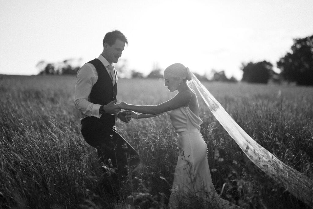 Black and white portrait of bride and groom holding hands in a field