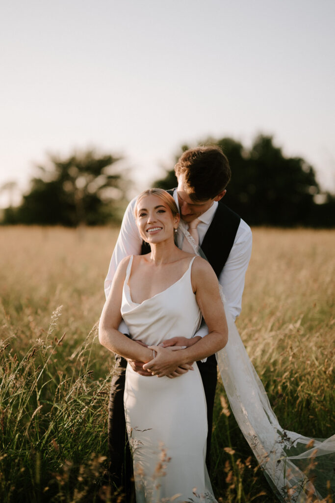 Groom standing behind bride during sunset countryside portraits